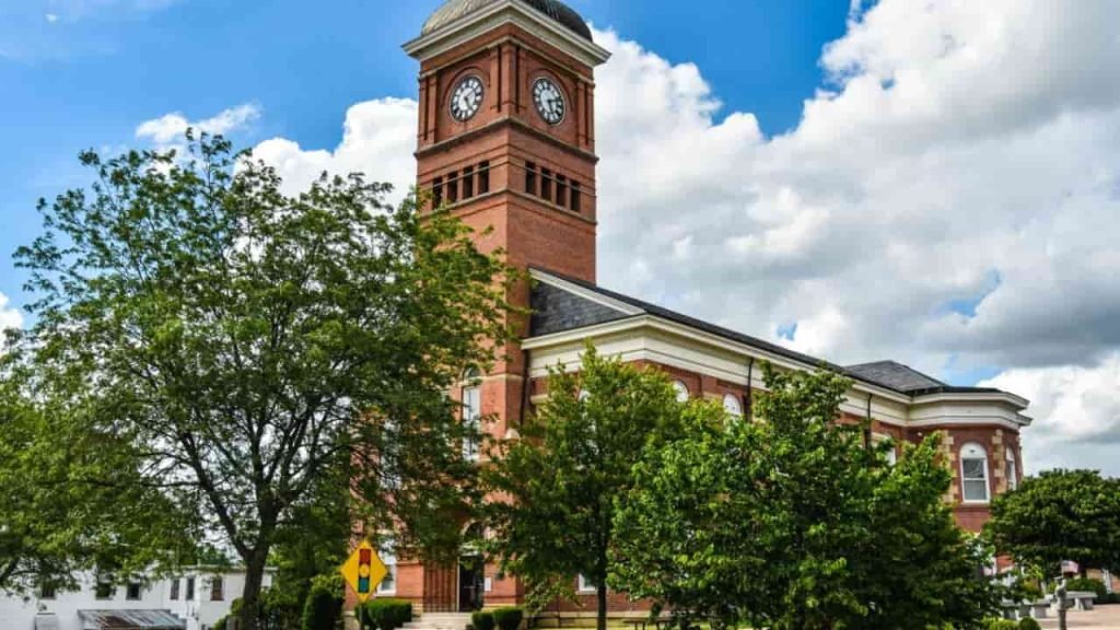 "Historic courthouse building in Morrow County Ohio with red brick clock tower, surrounded by green trees under a bright blue sky."
